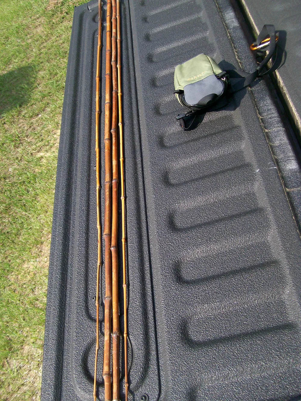 Several long bamboo cane poles laid side by side on the tailgate of a pickup truck, a small tackle bag beside them