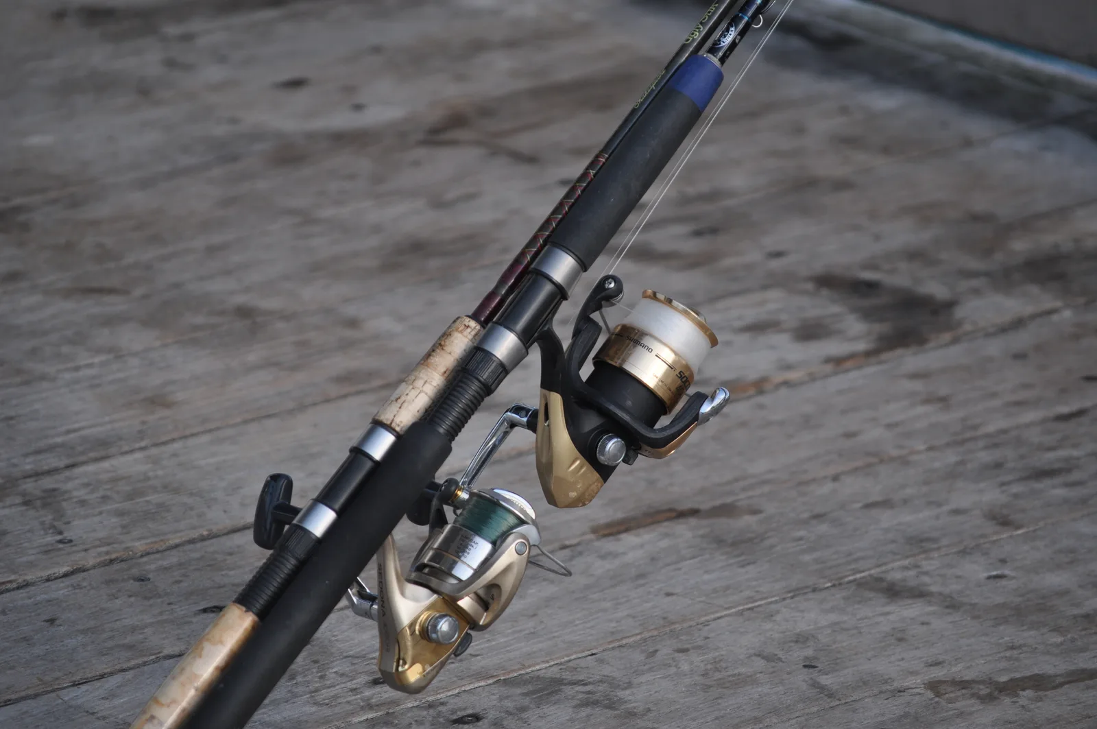 Two spinning reels on heavy rods lying on the planks of a Florida fishing pier