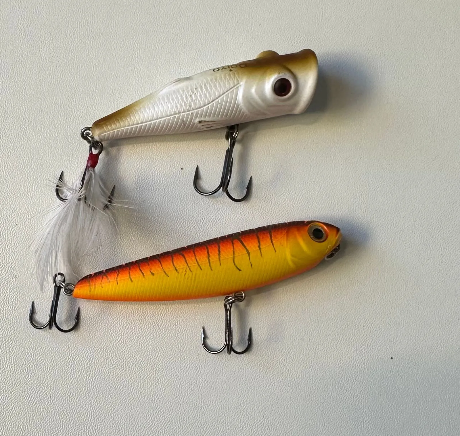 Two hard-bodied topwater plugs with treble hooks, one white and one orange